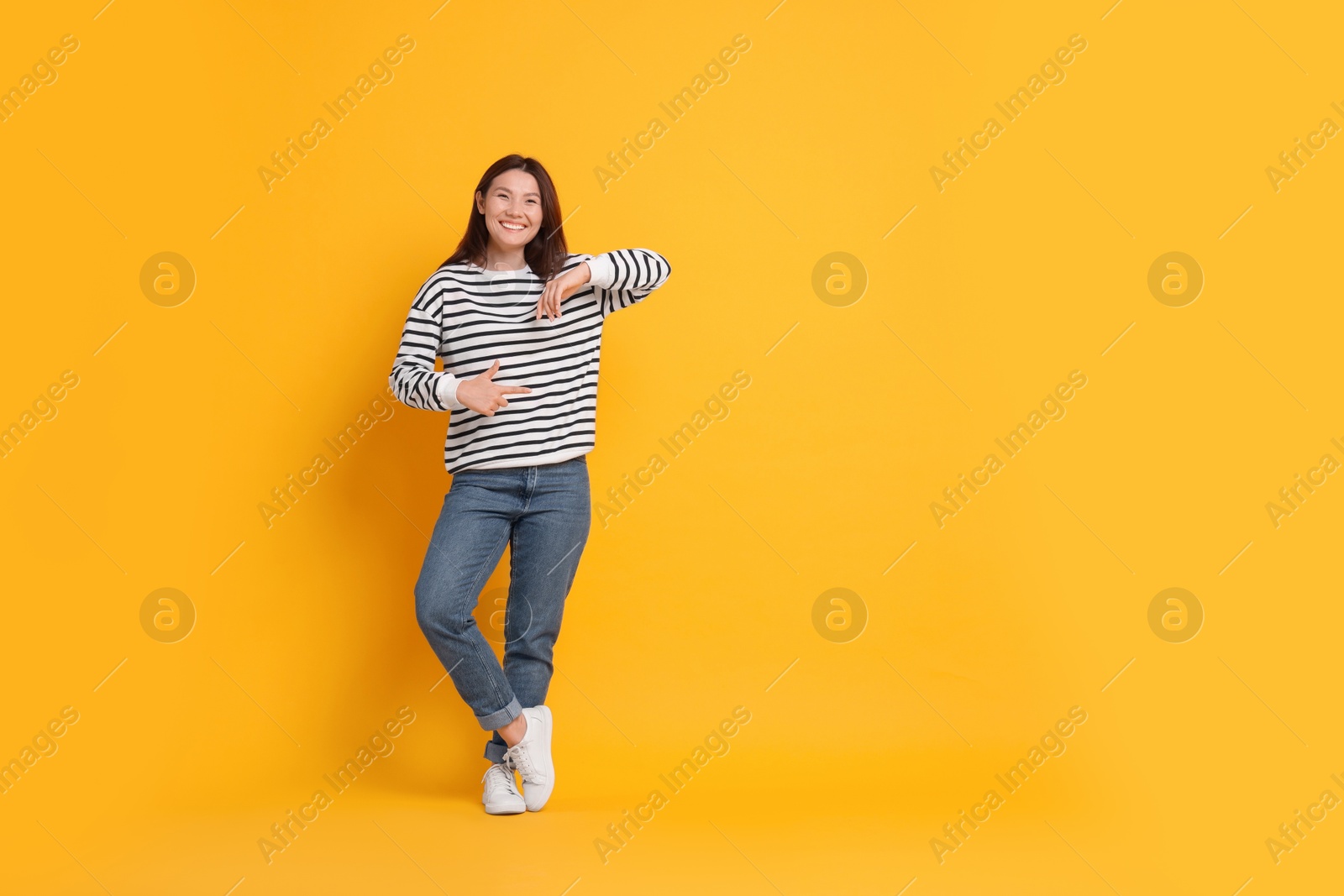 Photo of Smiling woman pointing at something on yellow background. Space for text