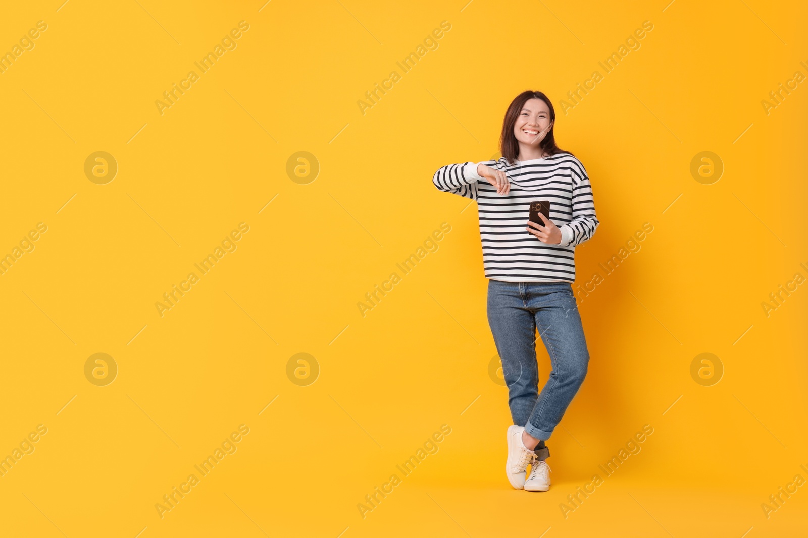 Photo of Smiling young woman with smartphone on yellow background. Space for text