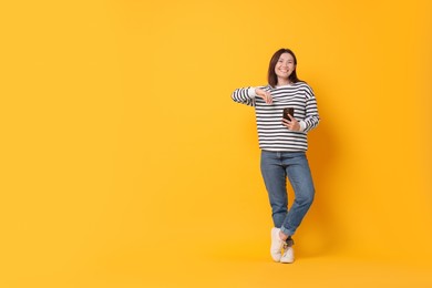 Photo of Smiling young woman with smartphone on yellow background. Space for text