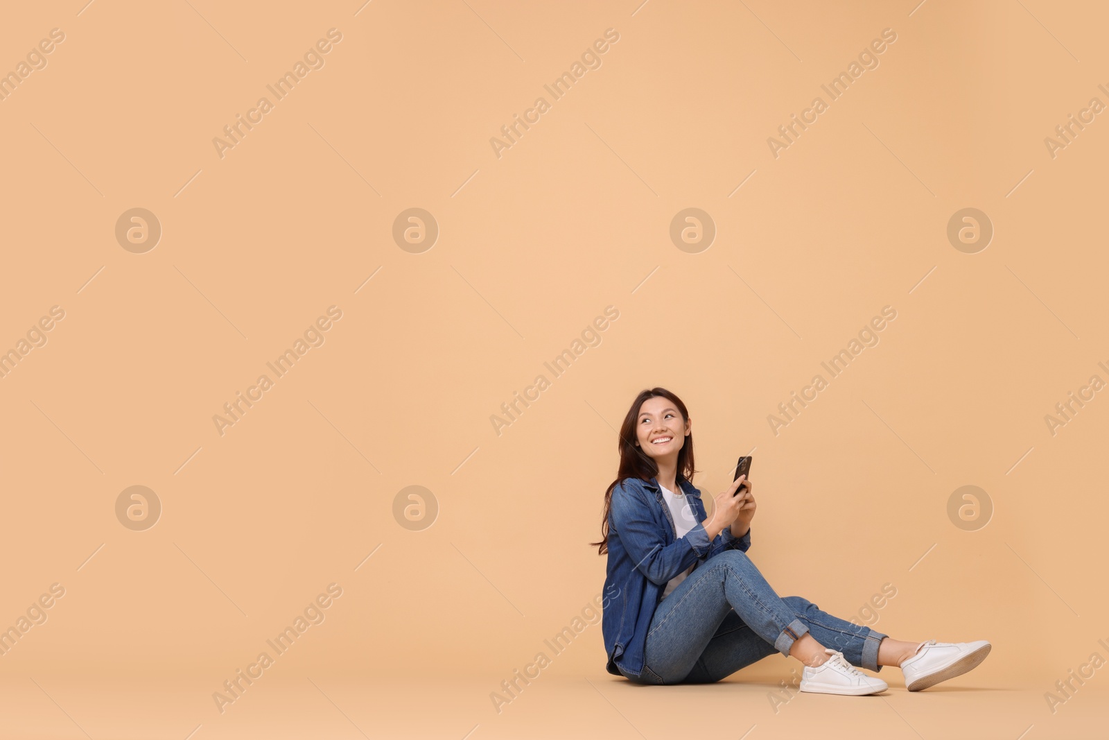 Photo of Smiling woman with smartphone on beige background. Space for text