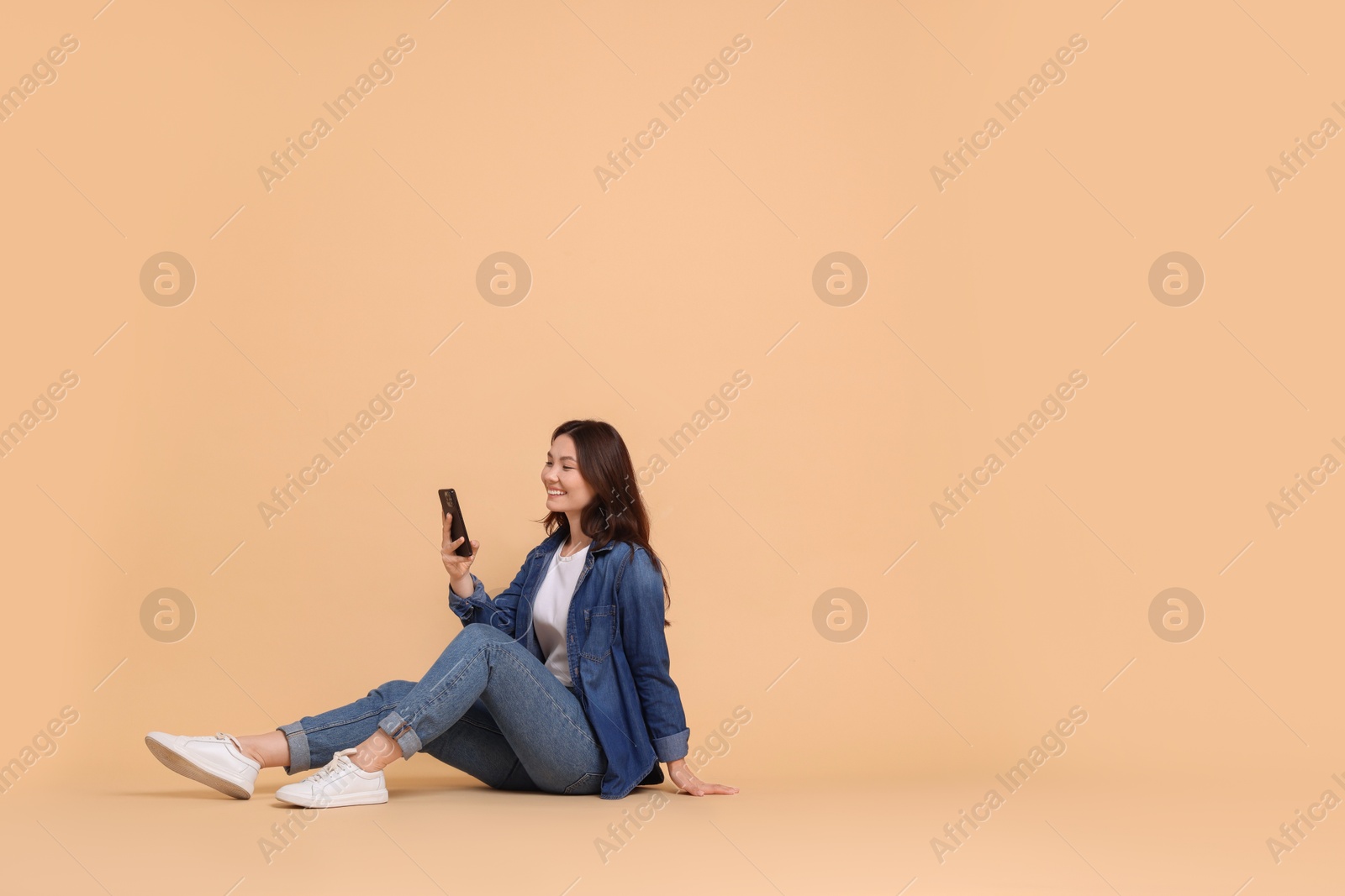 Photo of Smiling woman using smartphone on beige background