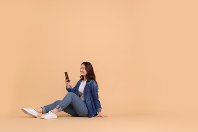 Photo of Smiling woman using smartphone on beige background