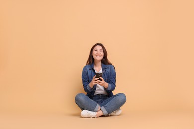 Smiling woman with smartphone on beige background