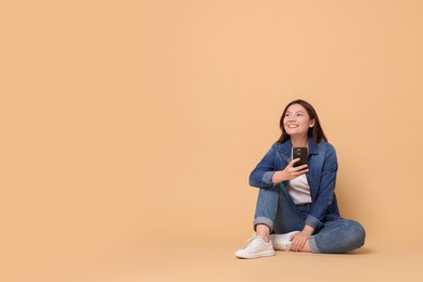 Photo of Smiling woman with smartphone on beige background. Space for text