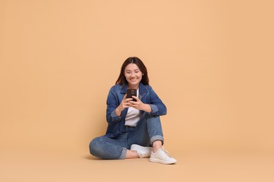 Photo of Smiling woman using smartphone on beige background