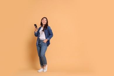 Photo of Smiling woman with smartphone on beige background. Space for text