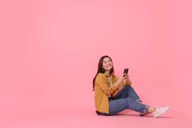 Smiling young woman with smartphone on pink background. Space for text