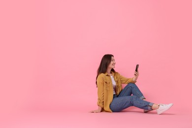 Photo of Smiling woman using smartphone on pink background. Space for text