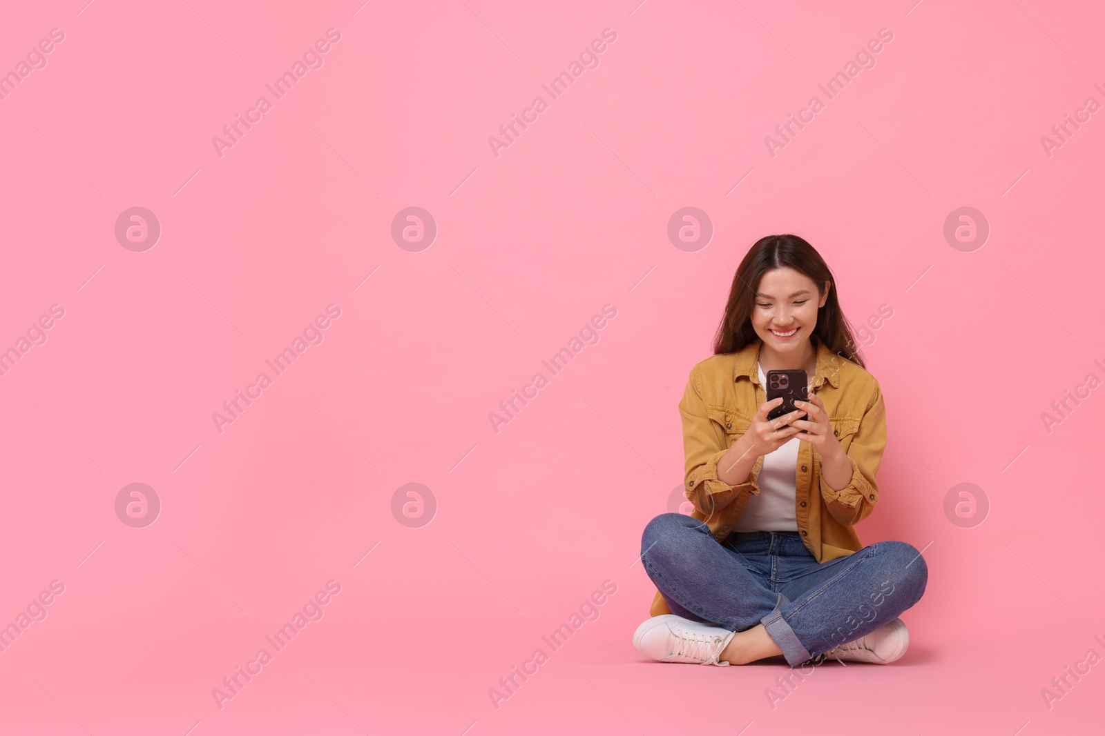 Photo of Smiling woman using smartphone on pink background. Space for text