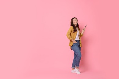 Photo of Smiling young woman with smartphone on pink background. Space for text