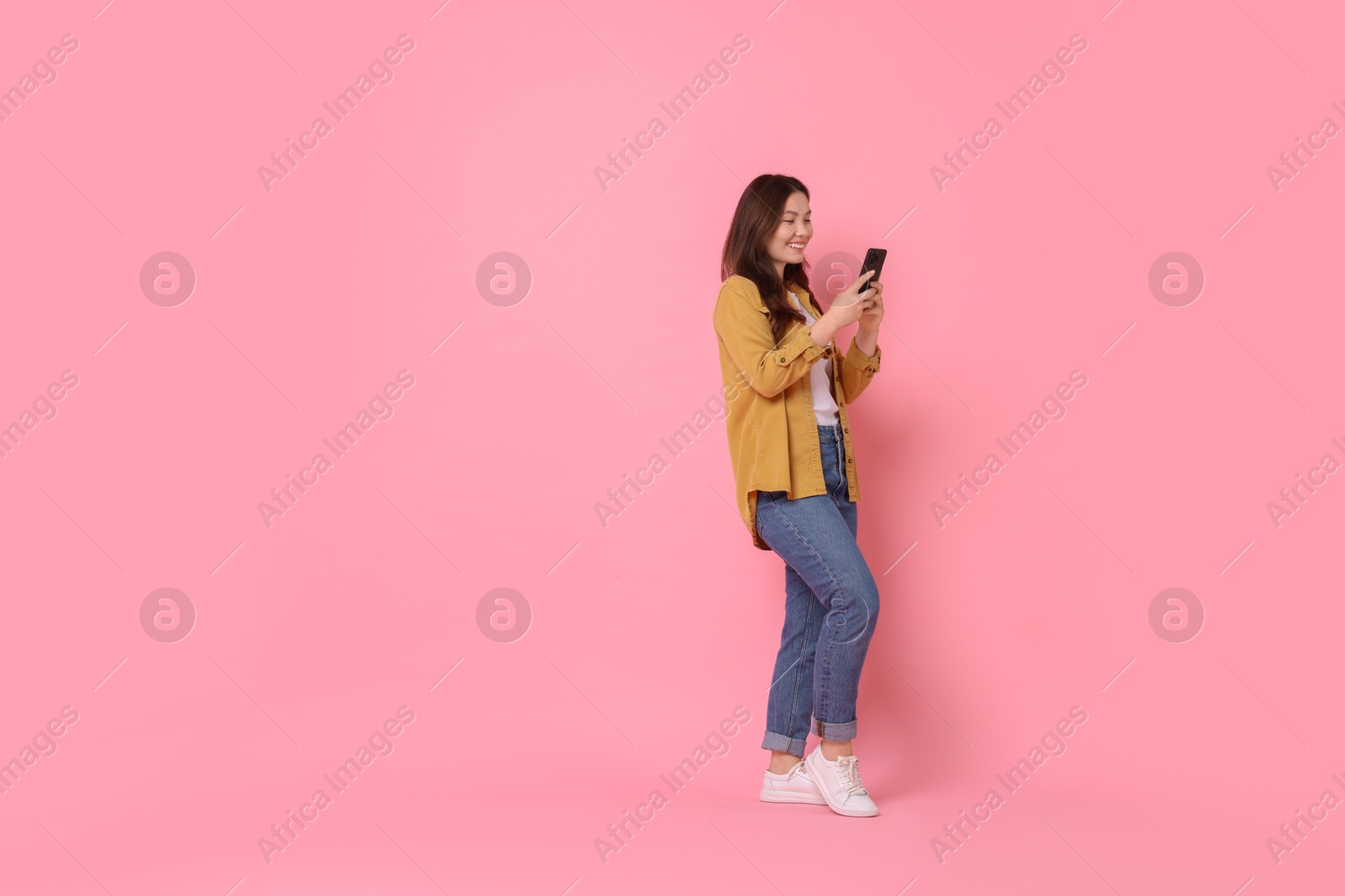 Photo of Smiling woman using smartphone on pink background. Space for text