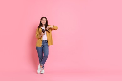 Photo of Smiling young woman with smartphone on pink background. Space for text