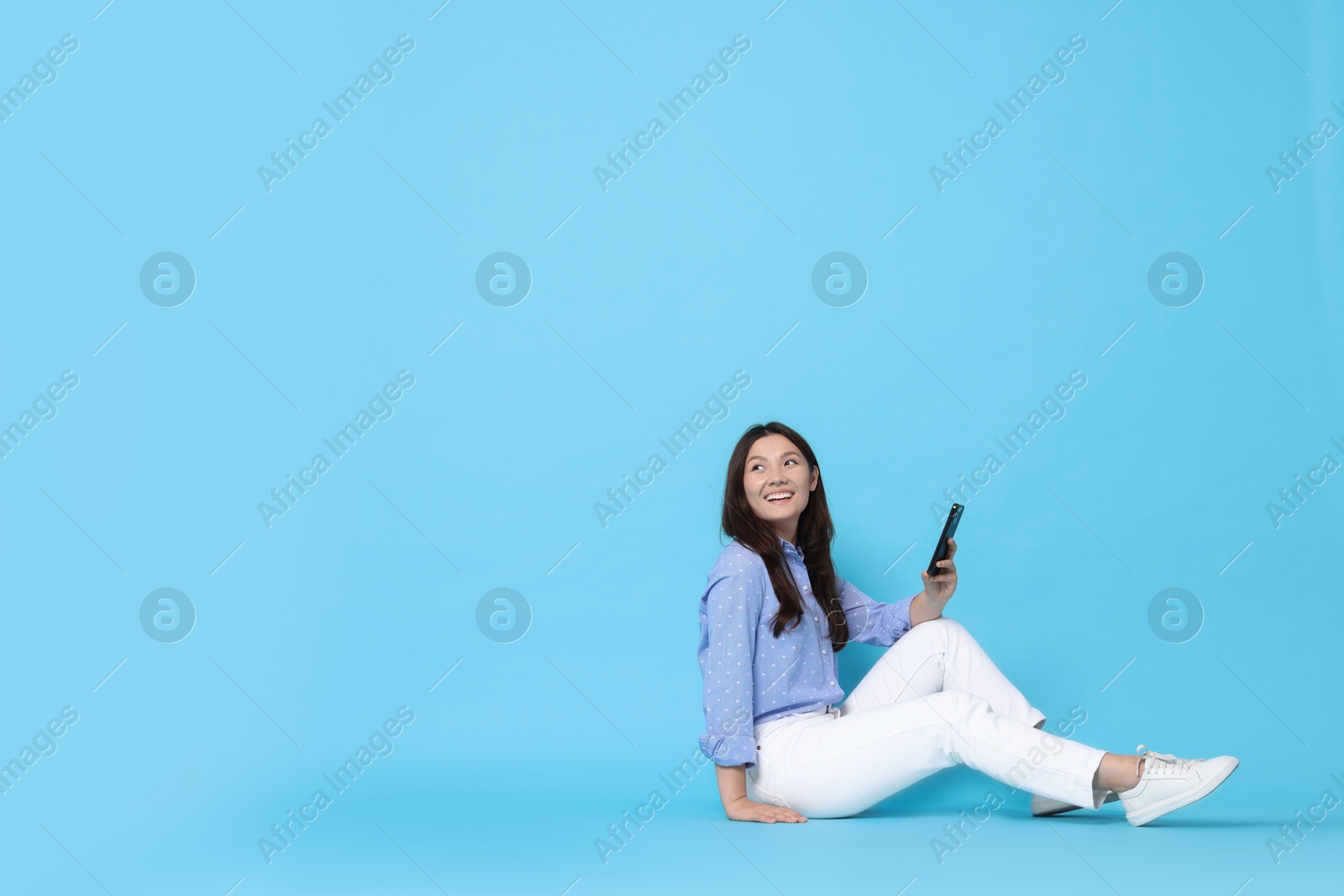 Photo of Smiling woman with smartphone on light blue background. Space for text