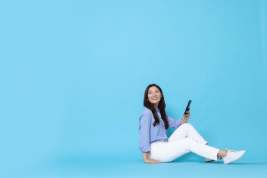 Smiling woman with smartphone on light blue background. Space for text