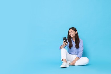 Smiling woman using smartphone on light blue background. Space for text