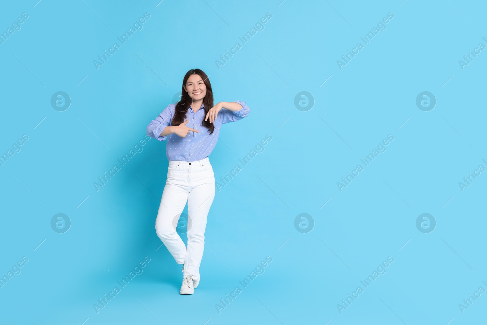 Photo of Smiling woman pointing at something on light blue background. Space for text