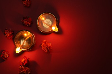 Photo of Diwali celebration. Diya lamps and beautiful flowers on red background, flat lay. Space for text