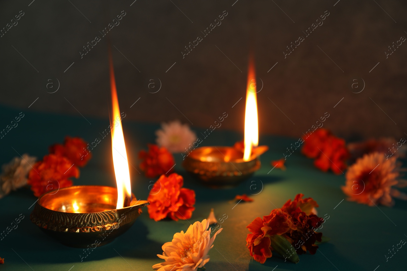 Photo of Diwali celebration. Diya lamps and beautiful flowers on teal table, closeup