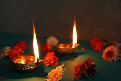 Photo of Diwali celebration. Diya lamps and beautiful flowers on teal table, closeup