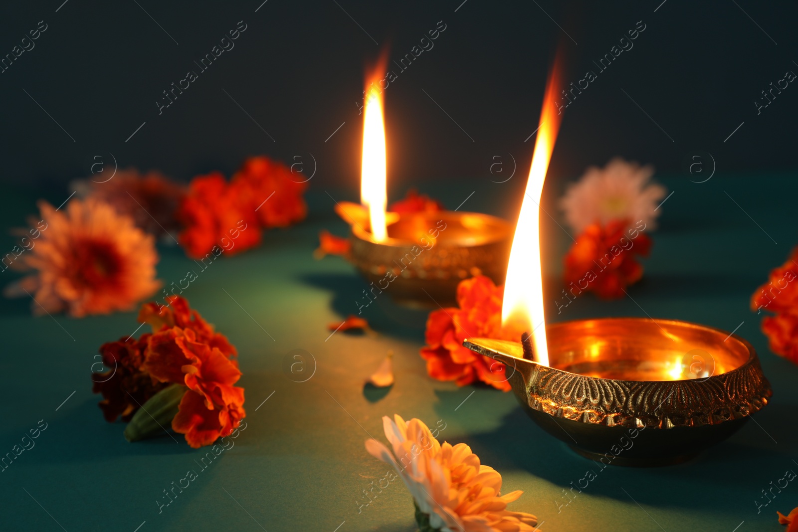 Photo of Diwali celebration. Diya lamps and beautiful flowers on teal table, closeup