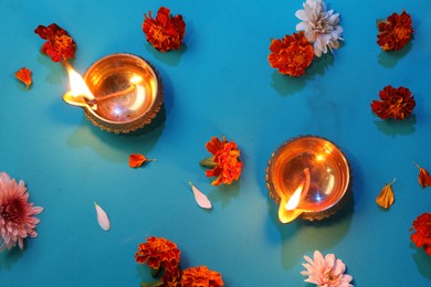 Photo of Diwali celebration. Diya lamps and beautiful flowers on blue background, flat lay