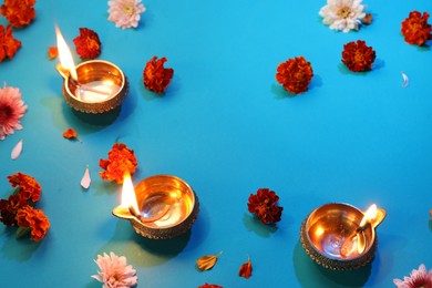 Photo of Diwali celebration. Diya lamps and beautiful flowers on blue background, above view