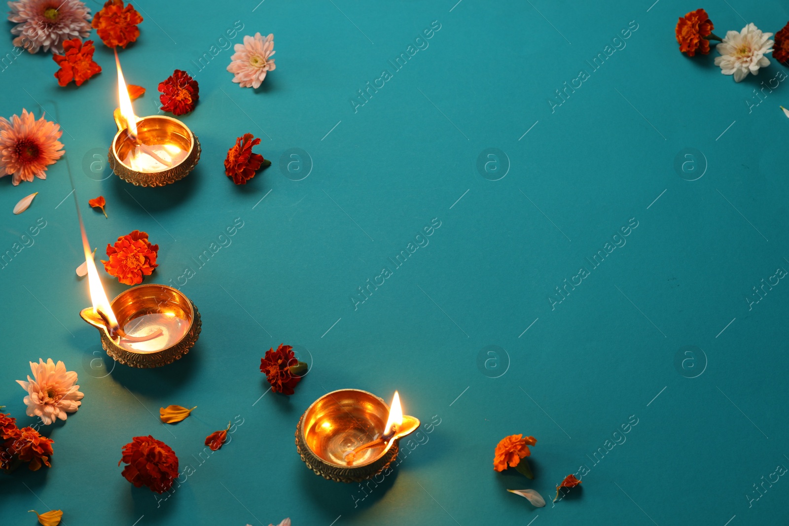 Photo of Diwali celebration. Diya lamps and beautiful flowers on teal background, flat lay. Space for text