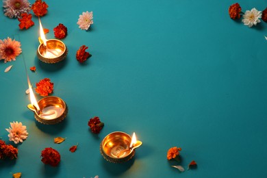 Photo of Diwali celebration. Diya lamps and beautiful flowers on teal background, flat lay. Space for text