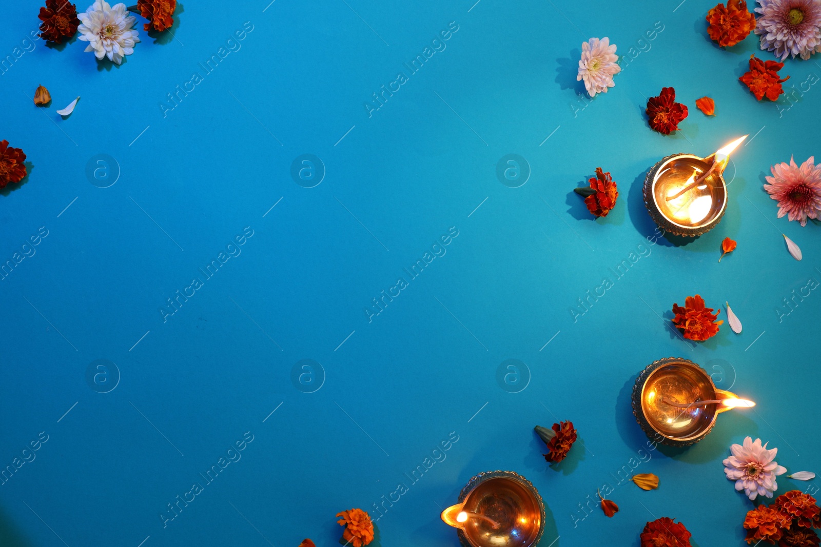 Photo of Diwali celebration. Diya lamps and beautiful flowers on blue background, flat lay. Space for text