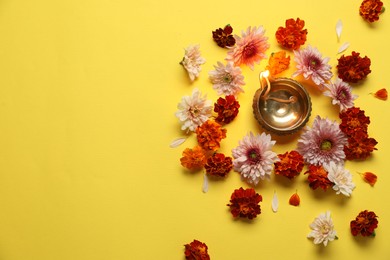 Photo of Diwali celebration. Diya lamp and beautiful flowers on yellow background, flat lay. Space for text