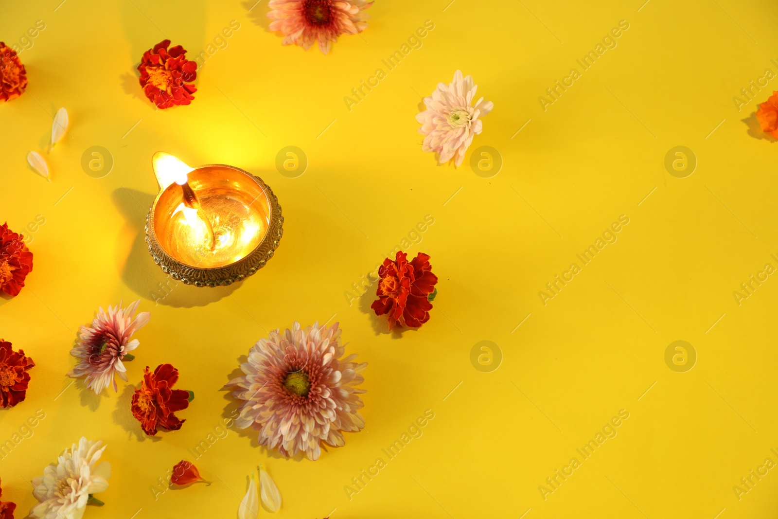 Photo of Diwali celebration. Diya lamp and beautiful flowers on yellow background, flat lay. Space for text