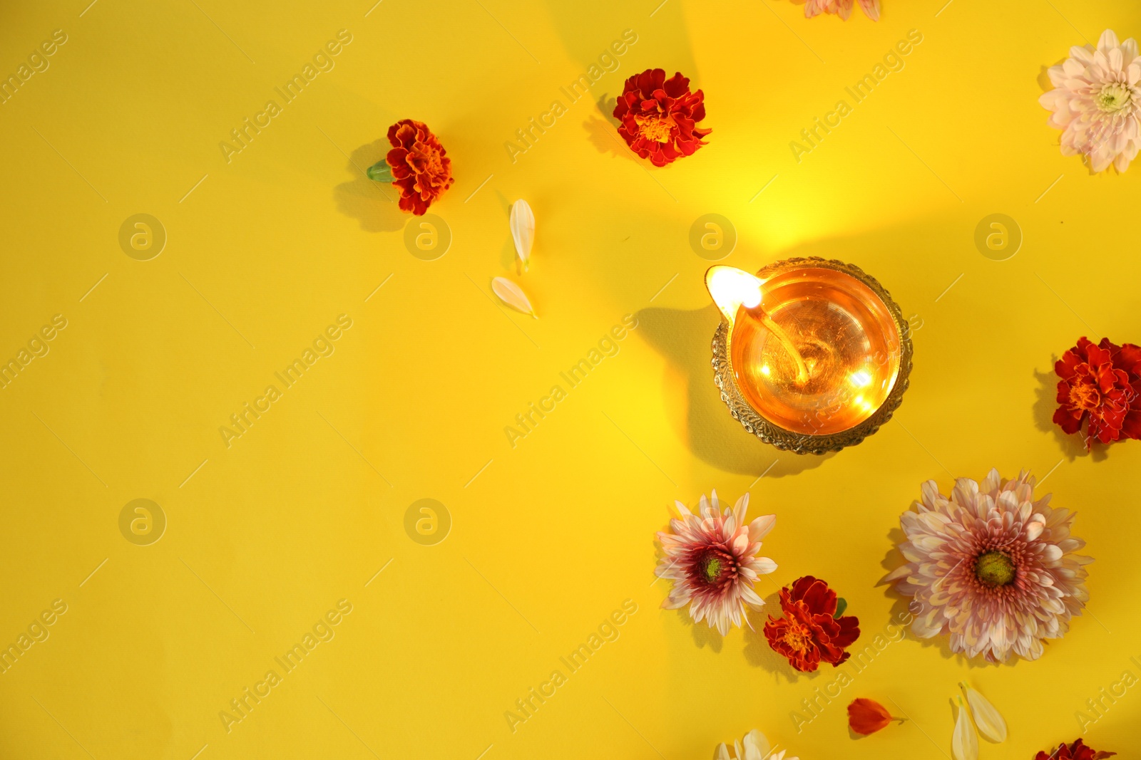 Photo of Diwali celebration. Diya lamp and beautiful flowers on yellow background, flat lay. Space for text