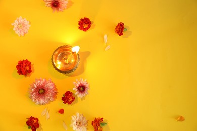 Photo of Diwali celebration. Diya lamp and beautiful flowers on yellow background, flat lay. Space for text