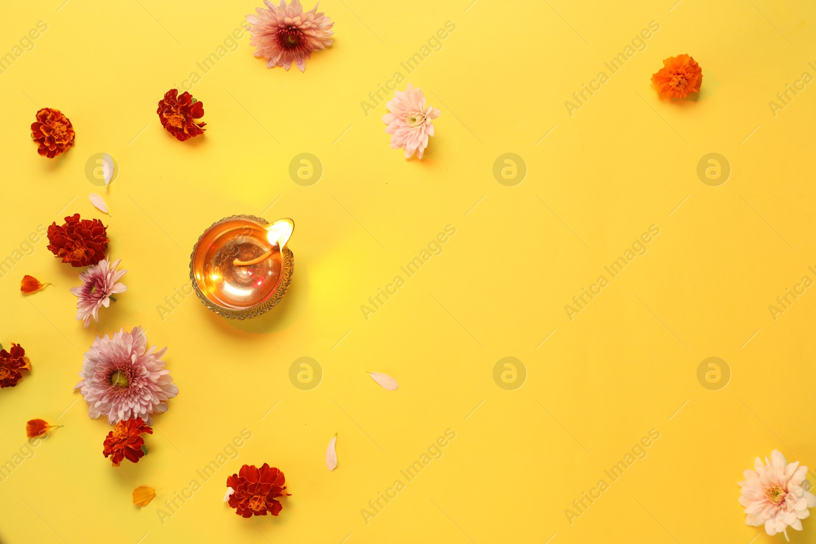 Photo of Diwali celebration. Diya lamp and beautiful flowers on yellow background, flat lay. Space for text