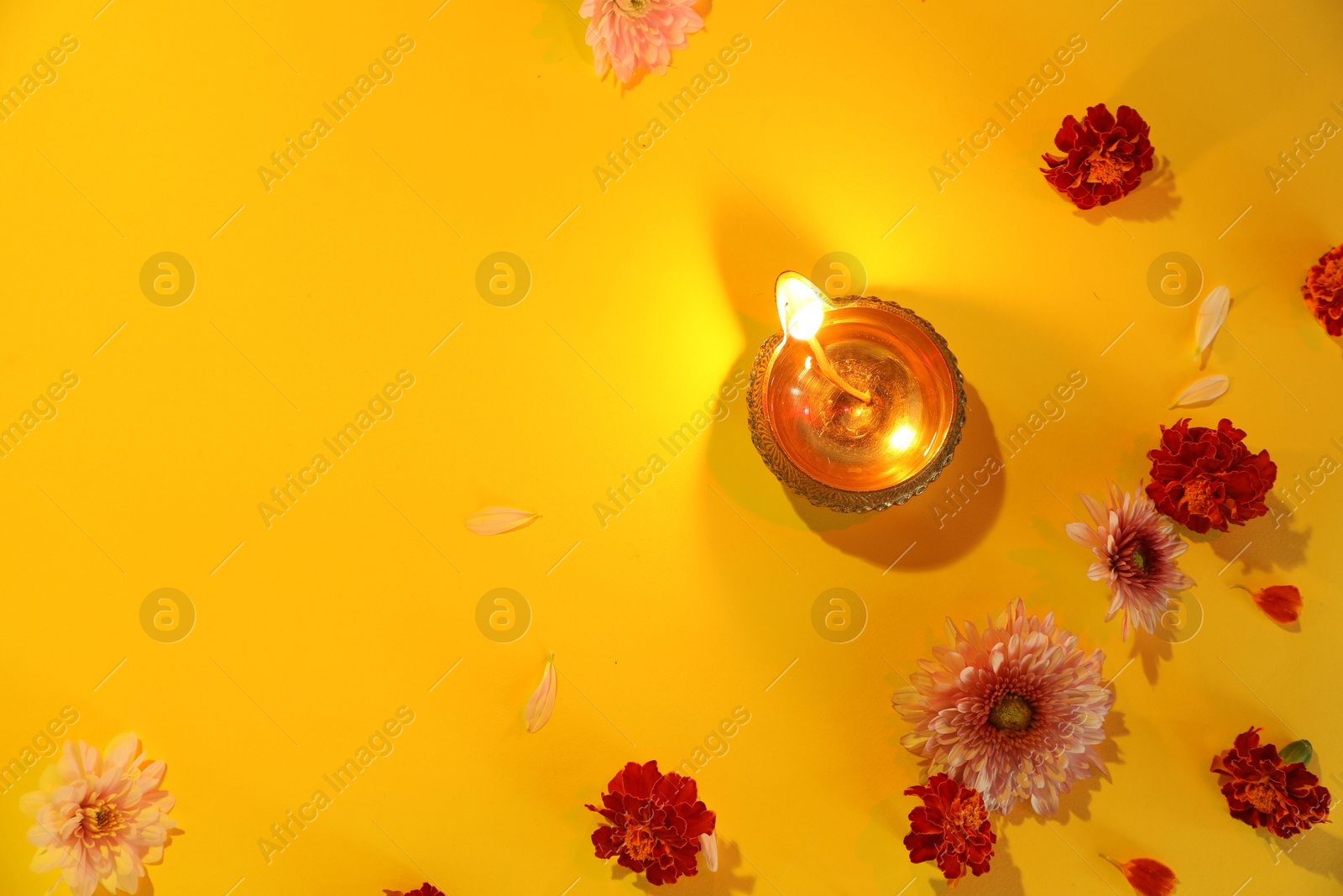 Photo of Diwali celebration. Diya lamp and beautiful flowers on yellow background, flat lay. Space for text