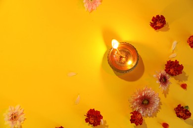 Diwali celebration. Diya lamp and beautiful flowers on yellow background, flat lay. Space for text