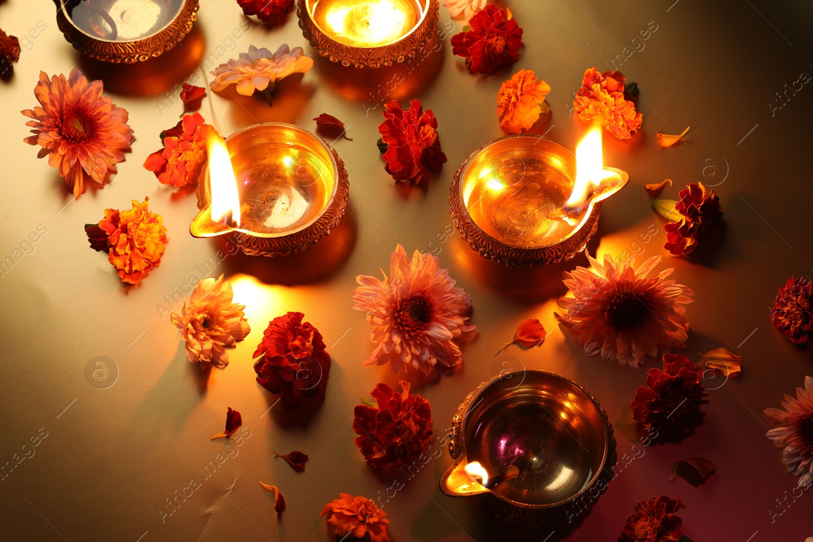 Photo of Diwali celebration. Diya lamps and beautiful flowers on golden background, above view