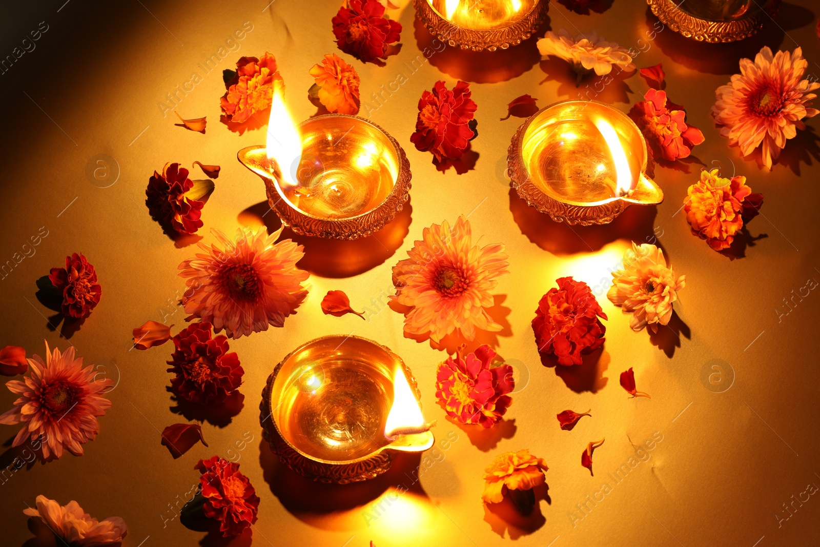 Photo of Diwali celebration. Diya lamps and beautiful flowers on golden background, above view