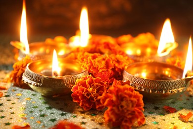 Photo of Diwali celebration. Diya lamps and beautiful marigold flowers on gray patterned surface, closeup