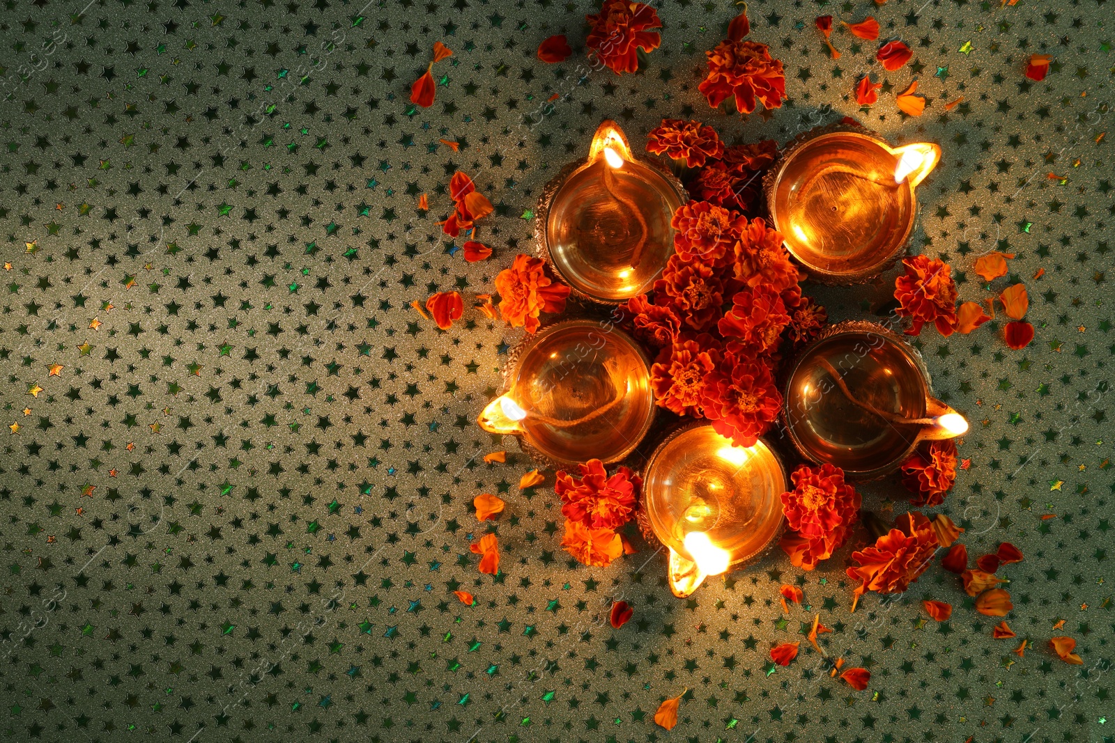 Photo of Diwali celebration. Diya lamps and beautiful marigold flowers on gray patterned surface, flat lay. Space for text