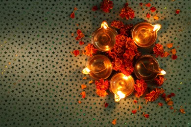 Diwali celebration. Diya lamps and beautiful marigold flowers on gray patterned surface, flat lay. Space for text