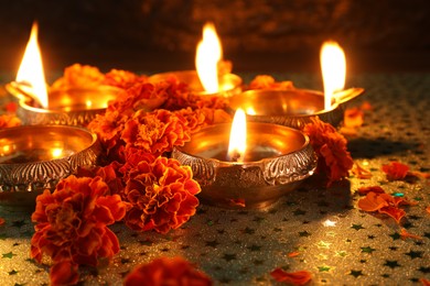 Photo of Diwali celebration. Diya lamps and beautiful marigold flowers on gray patterned surface, closeup