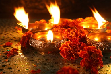 Diwali celebration. Diya lamps and beautiful marigold flowers on gray patterned surface, closeup