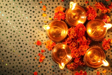 Photo of Diwali celebration. Diya lamps and beautiful marigold flowers on gray patterned surface, flat lay. Space for text