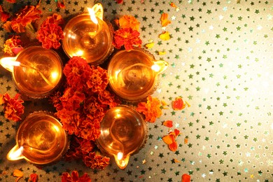 Diwali celebration. Diya lamps and beautiful marigold flowers on gray patterned surface, flat lay. Space for text