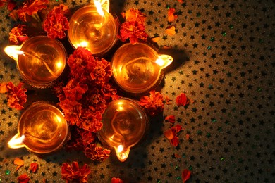 Diwali celebration. Diya lamps and beautiful marigold flowers on gray patterned surface, flat lay. Space for text