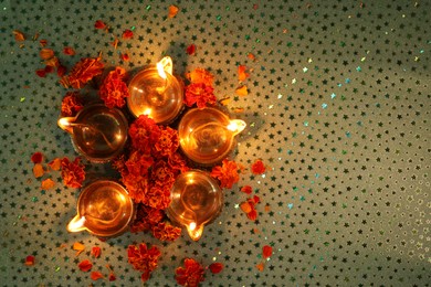 Photo of Diwali celebration. Diya lamps and beautiful marigold flowers on gray patterned surface, flat lay. Space for text