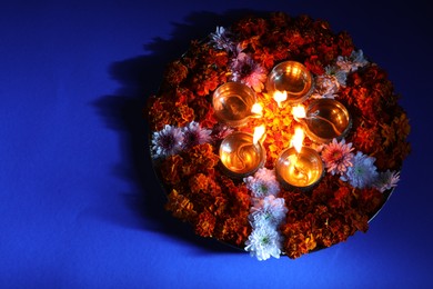 Photo of Diwali celebration. Diya lamps and beautiful flowers on blue background, top view