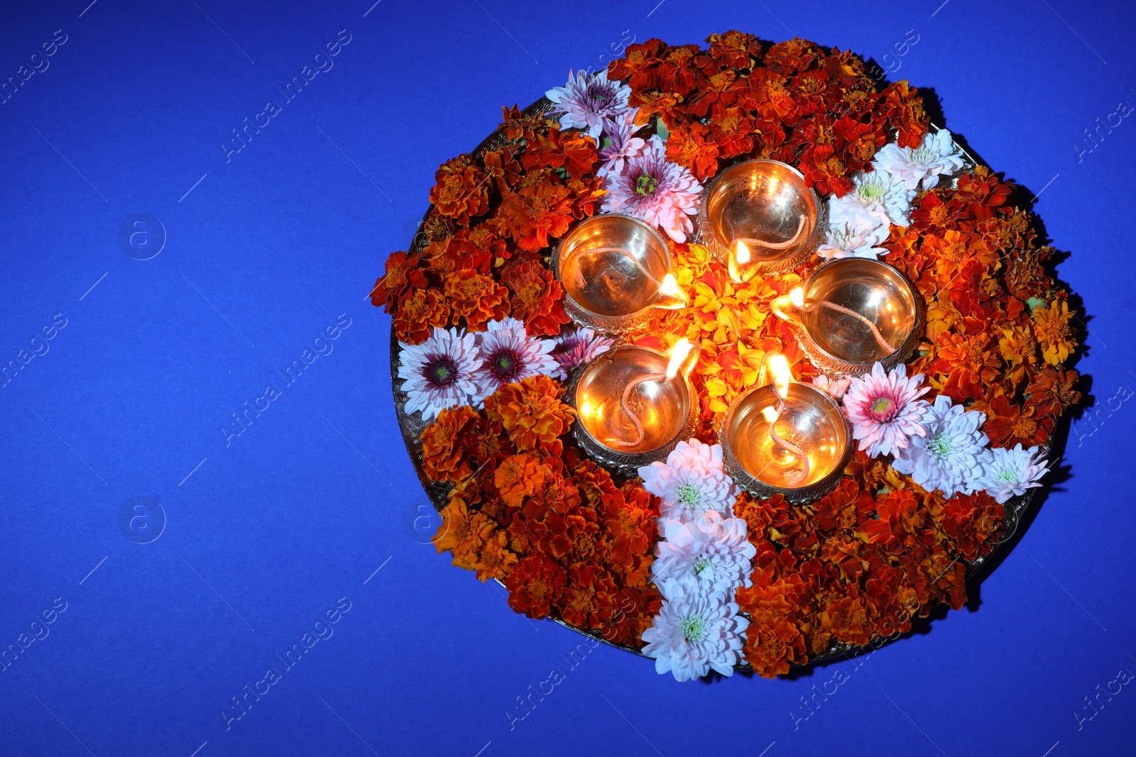 Photo of Diwali celebration. Diya lamps and beautiful flowers on blue background, top view. Space for text