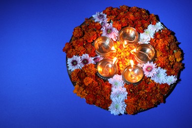 Diwali celebration. Diya lamps and beautiful flowers on blue background, top view. Space for text